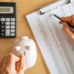 Woman inserting coin in piggy bank and checking spreadsheet of home finances using calculator, managing monthly budget and saving for future